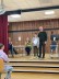 Die Schulleitung und ein Schüler stehen auf der Bühne. Der Schüler hält eine Urkunde in der Hand.