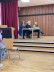 Jury (bestehend aus 3 Personen) sitzt auf Stühlen vor einem Tisch auf der Bühne 