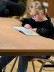 junge Schülerin sitzt an einem Tisch und liest aus einem Buch vor 