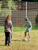 Zwei Kinder spielen Blindenfußball auf einer Wiese, wobei ein Kind eine Augenbinde trägt 