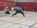 Junge rollt einen Klingelball über den Boden einer Turnhalle 