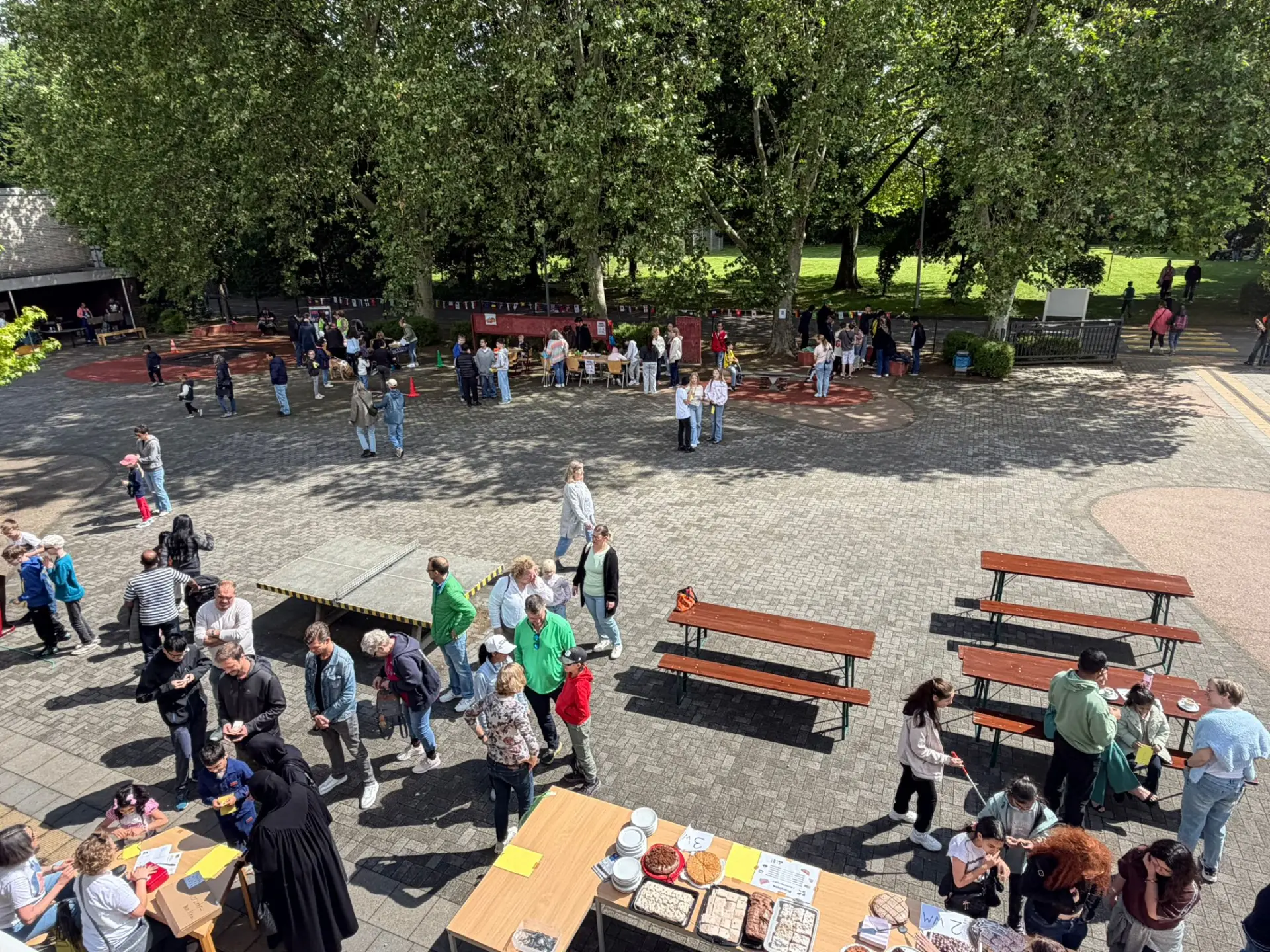 Das Schulgelände ist voller Besucherinnen und Besucher, die an verschiedenen Ständen und Aktionen des Sommerfests teilnehmen.