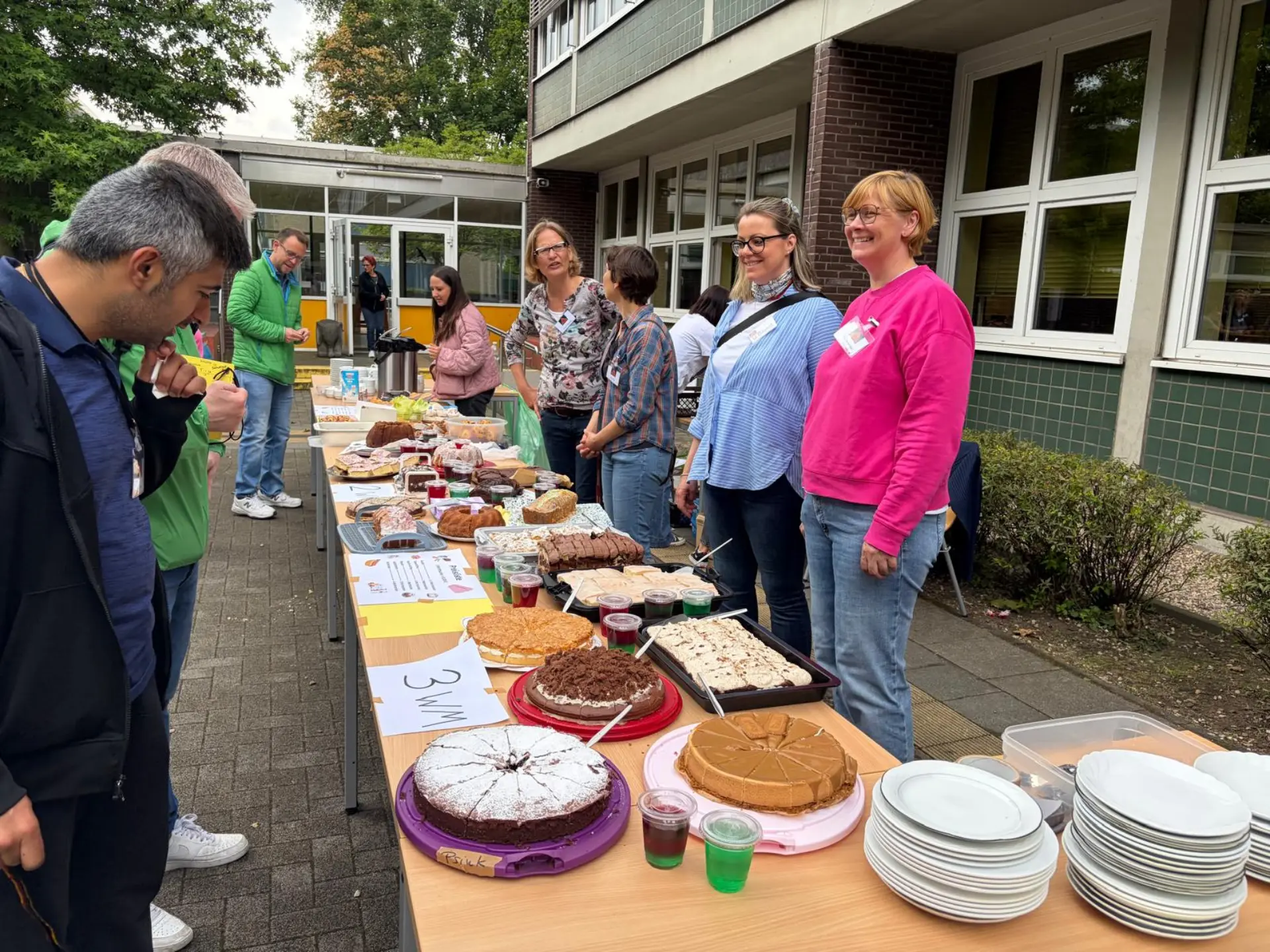 Mehrere erwachsene Personen stehen hinter einem Tisch, auf dem verschiedene Kuchen und Torten stehen 
