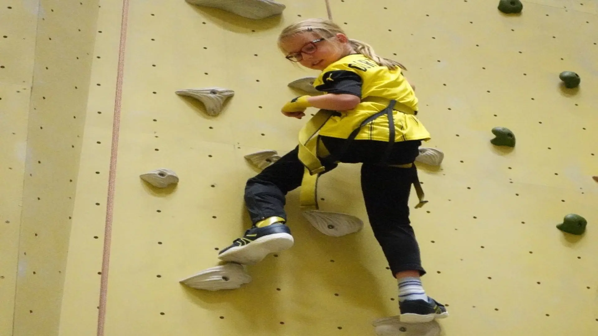 Schülerin klettert abgesichert eine Kletterwand hoch. 