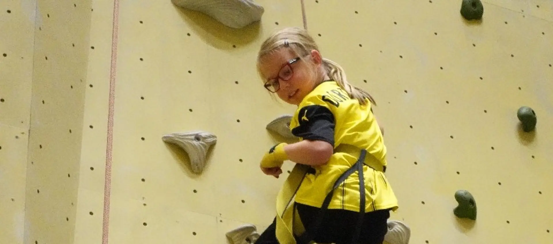 Eine Schülerin klettert abgesichert eine Kletterwand hoch. 