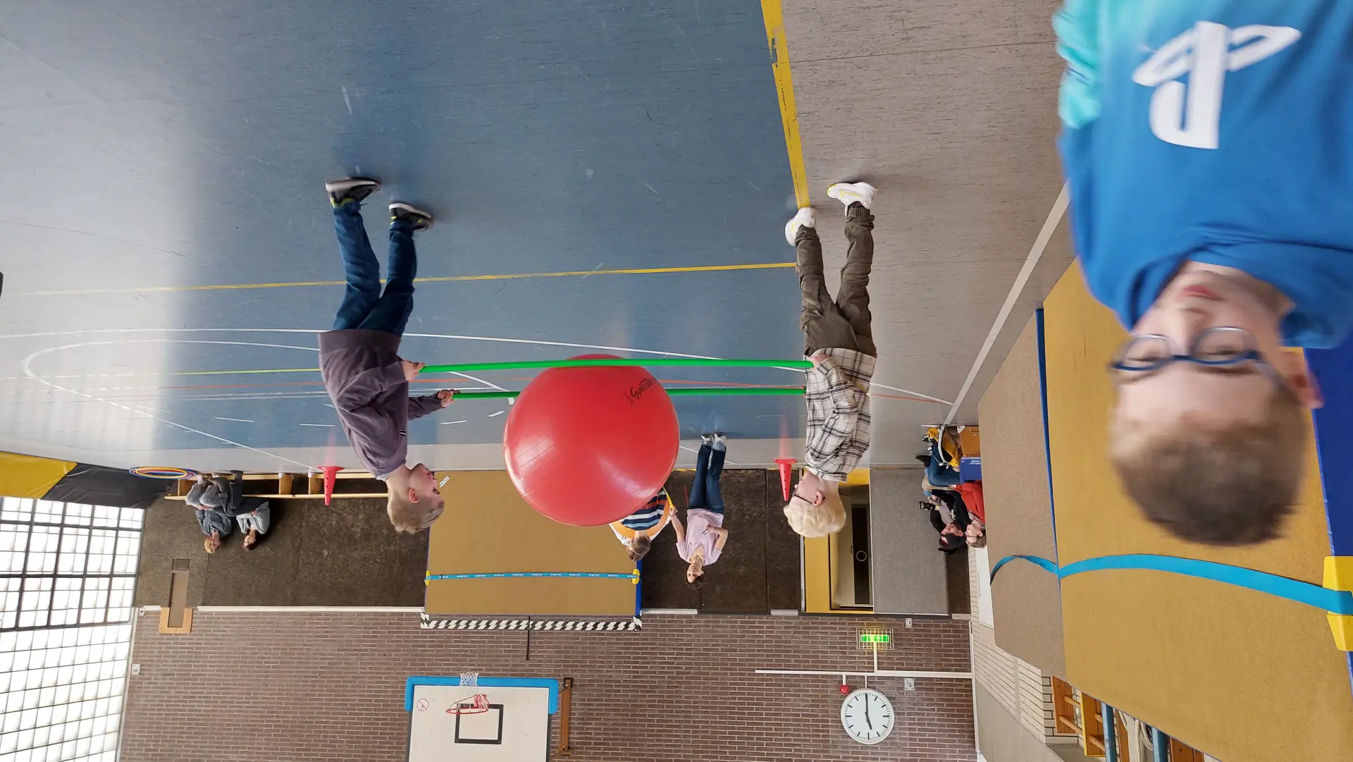 Mehrere Schüler:innen spielen mit einem großen Ball in einer Sporthalle 