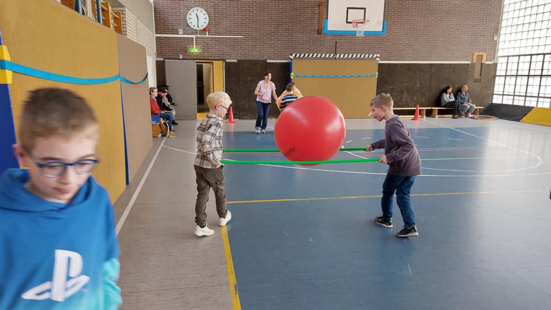 Mehrere Schüler:innen spielen mit einem großen Ball in einer Sporthalle 