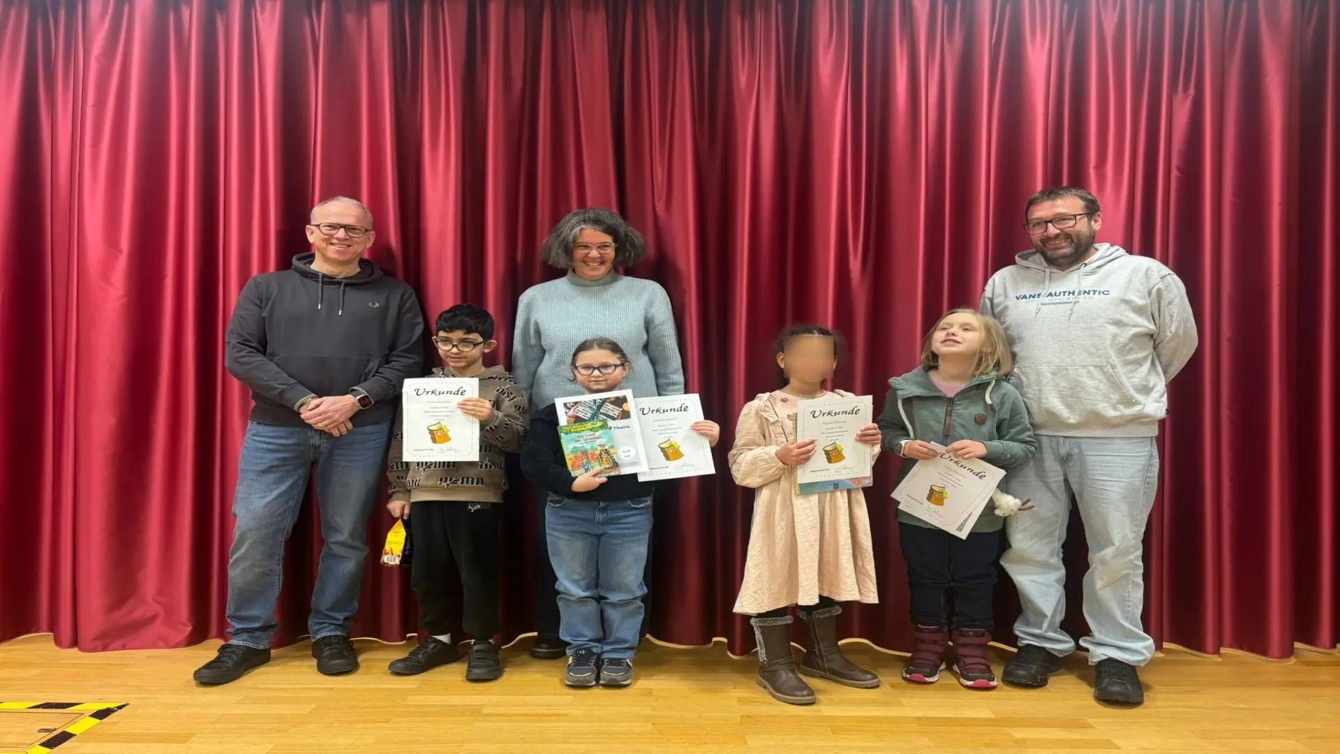 Mehrere Personen stehen gemeinsam auf der Bühne. Die Schüler:innen halten stolz ihre Urkunden in den Händen. 