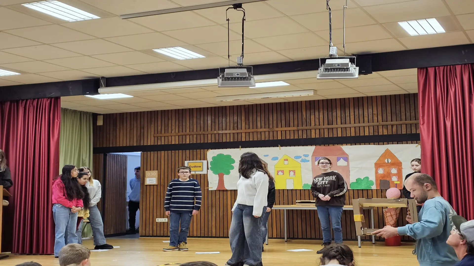 Mehrere Schülerinnen und Schüler stehen auf der Bühne und führen ein Theaterstück auf. 