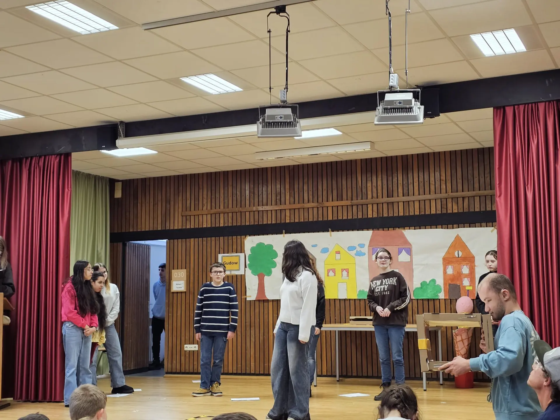 Mehrere Schülerinnen und Schüler stehen auf der Bühne und führen ein Theaterstück auf. 