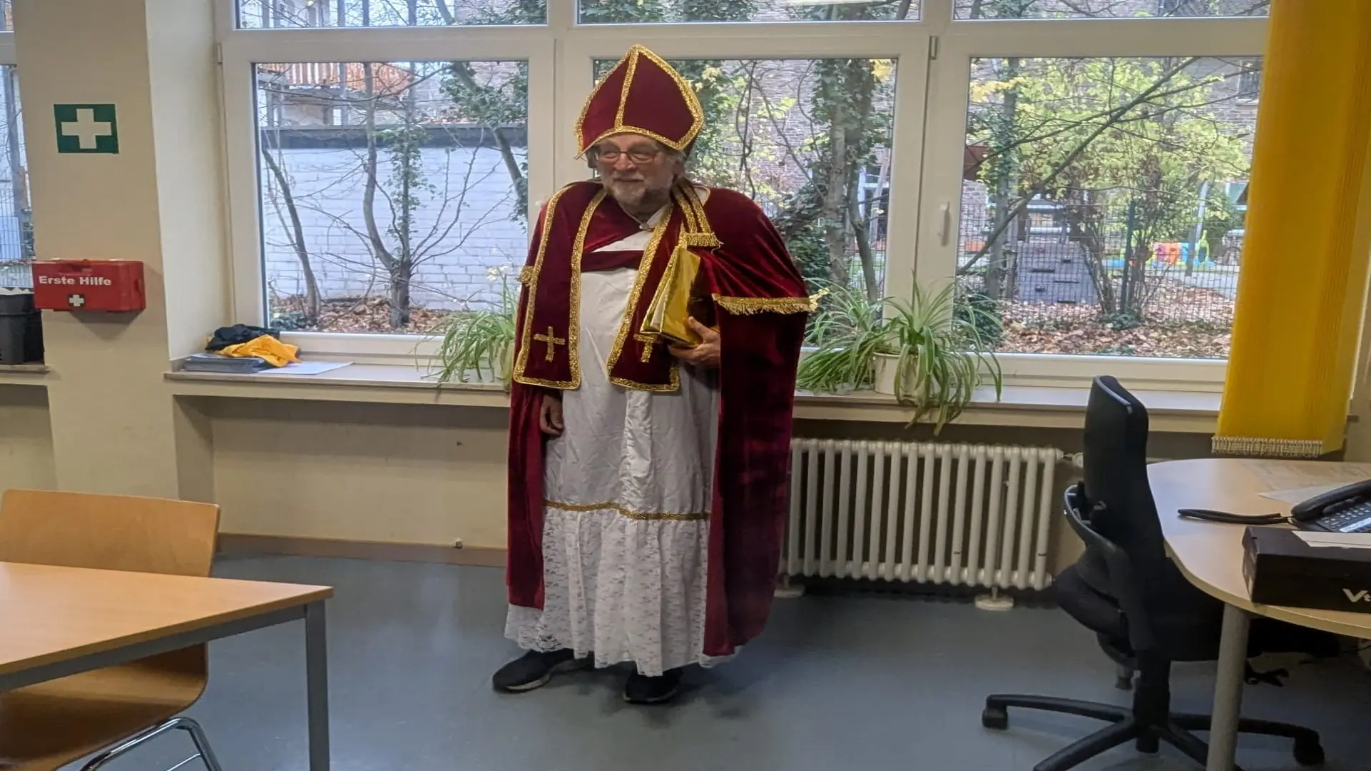 Ein älterer Herr steht, in ein Nikolauskostüm gekleidet, vor einer Fensterbank.