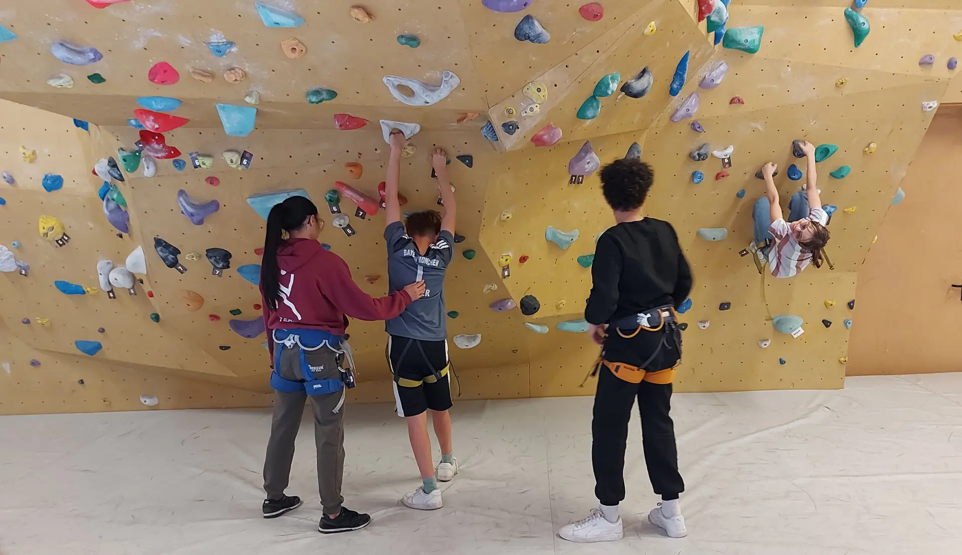 Vier Jugendliche vor einer bunten Boulderwand in einer Kletterhalle